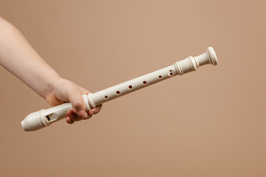 Hold ivory color common fipple flute with one hand closeup, beige background. Woodwind musical instrument. Aerophone or reedless wind instrument that produce sound from flow of air across opening.
