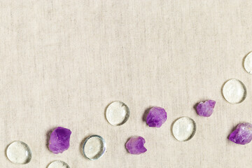Flat lay from purple amethyst crystals and glass stones on textile background with copy space,  top view natural gemstone. Amethyst stone healing crystal, rocks quartz mineral close up