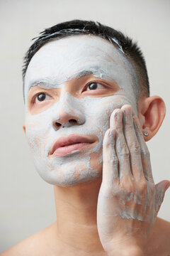 Serious young man gently wiping dry detoxifying clay mask off face