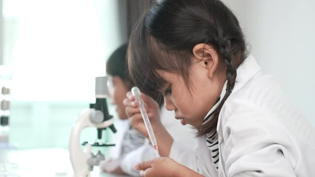 Slow motion shot, Selective focus, little girl use dropper liquid on plate test, Two asian siblings wearing coat learning experimenting with liquids, while studying science chemistry
