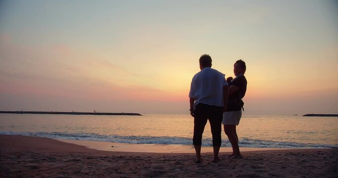 Happy Multi generation Asian family enjoying standing on Ocean sea beach sunrise and dramatic colorful sky in the morning, holiday vacation with Family enjoy and having fun outdoor activity lifestyle