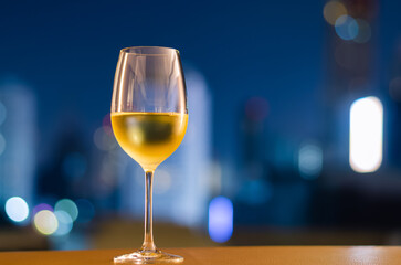 A glass of white wine puts on table at balcony with blurred city background. Relaxing at home concept.