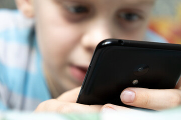 The boy lies on the bed and corresponds in a smartphone.