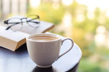 Selective focus of a white cup coffee puts on table at balcony with book and spectacles. Relaxing...