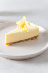 Piece of Classic New York Cheesecake with vanilla flower on white Concrete Background, side View, close up. Confectionery menu, sweet dessert recipe