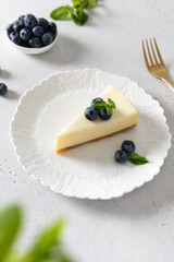 Delicious Piece of Classic New York Cheesecake with fresh blueberries and mint on white Concrete Background, side View, close up. Confectionery menu, sweet dessert recipe
