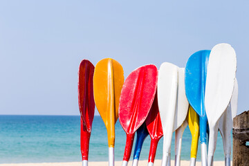 Colorful old oars over blurred beach background, summer outdoor day light, multi colour paddles