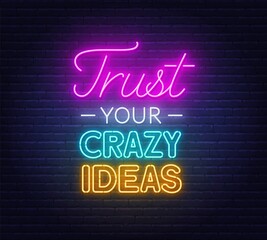 Trust Your Crazy Ideas neon lettering on brick wall background.
