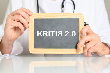 Ein Arzt am Schreibtisch mit einer Tafel auf der KRITIS 2.0 steht. Konzept Cyber Security für Krankenhäuser und Kliniken
