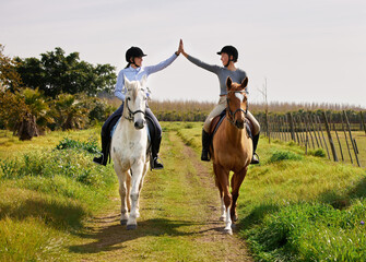 Youre doing great. Full length shot of two young woman high fiving while riding their horses on the...