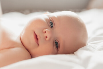 closeup portrait of a blue-eyed newborn baby lying on his back on a white sheet. happy carefree...