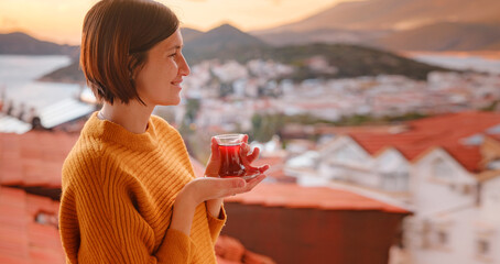 Woman drinking turkish tea from traditional turkish teacup and enjoys panorama over sunset of Kas...