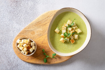 Fresh broccoli soup with croutons and micro green in a bowl on a gray background. Spring vegan...