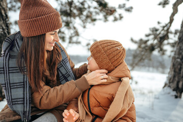 Young woman with a son in winter forest on a picnic drink hot tea