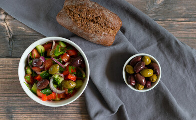 Vegan salad with kalamata olives on wooden background with gray textile.