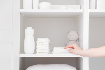 Young adult mother hand taking white towel from inside wardrobe. Bottle of talcum powder, stack of...