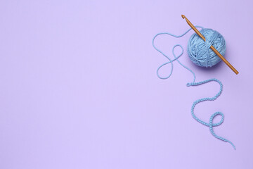 Clew of light blue knitting thread and crochet hook on violet background, top view. Space for text