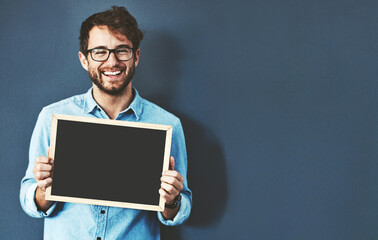 Have you heard about this before. Studio portrait of a young man holding a blackboard against a grey background.