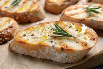 Tasty bruschettas with oil and rosemary on parchment paper, closeup