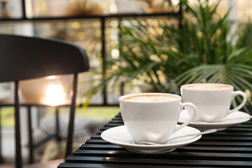 Ceramic cups of aromatic coffee with foam on wooden table in cafe