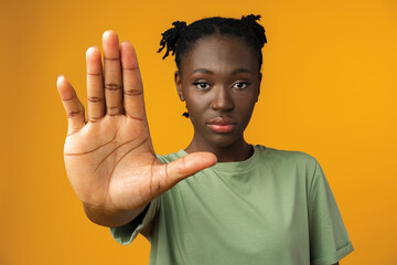 Portrait of a serious young african woman showing stop gesture in yellow studio - obrazy, fototapety, plakaty