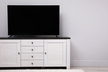 Modern TV on cabinet near white wall in room. Space for text