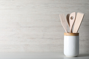 Holder with different kitchen utensils on white wooden table. Space for text