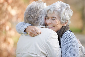 Friendship thats built to last. Two senior ladies embracing with autumn shaded trees in the background.