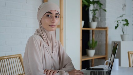 A woman in a hijab works in the office, freedom of choice of work for Muslim women. A beautiful woman sits at a computer and looks into the camera. New realities of the Islamic world.