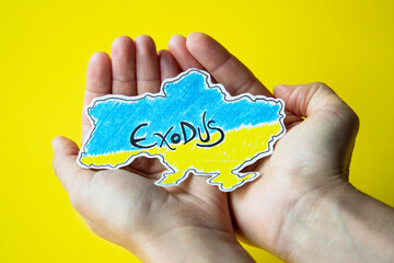 woman's hands hold the map of ukraine painted in the colors of its flag with the word exodus...