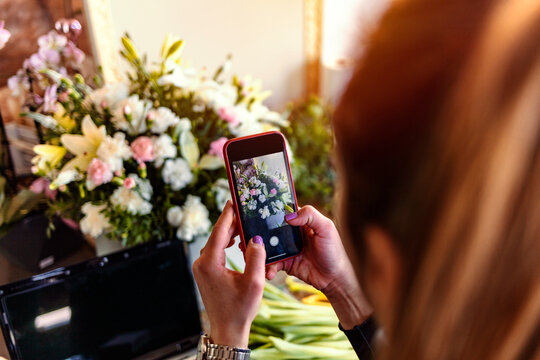Point of view of a florist taking a picture of a wreath on a smartphone for social media. Close up of a young woman using a phone to take a photo of her arrangement, while working in a flower shop.