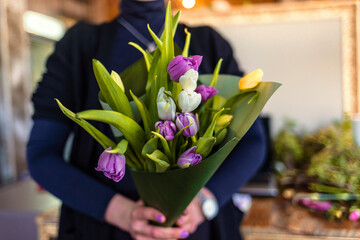 Young woman owner, seller, holds fresh bouquet of tulips in flower shop, cropped, copy space. Spring holidays, seasonal plants for trendy bouquet, delivery composition for client.