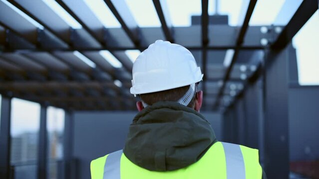 Architect worker in a hard hat helmet inspects the real estate building finished contraction project walking under the metal constructions.