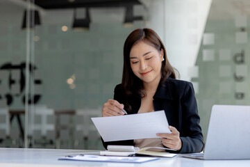 A beautiful Asian businesswoman sitting in her private office, she is checking company financial documents, she is a female executive of a startup company. Concept of financial management.