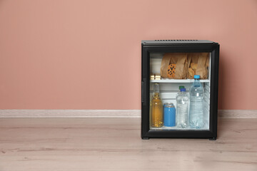 Mini bar filled with food and drinks near pale pink wall indoors, space for text