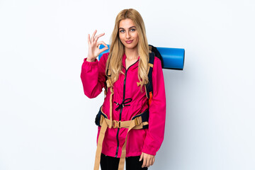 Young mountaineer woman with a big backpack over isolated white background showing an ok sign with fingers