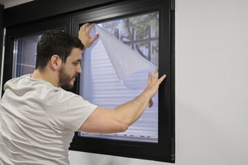 Young latin man installing frosted window vinyl on window glass.
