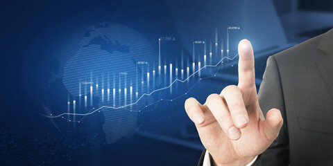 Close up of businessman hand pointing at abstract glowing business chart with globe hologram on blurry blue office workplace background. Trade, finance and economy concept. Double exposure.