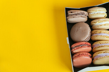 Multi-colored macaroons in a box on a yellow background. Top view, natural light. Selective focus with copy space