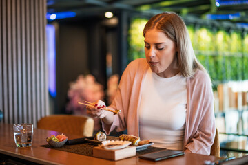Young woman is eating sushi with chopsticks at sushi restaurant.