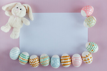 Easter eggs in pastel colors with a pattern and white toy rabbit on a pink-blue background