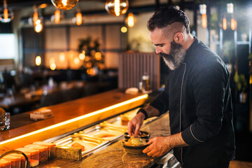 Sushi chef preparing dessert at sushi bar.