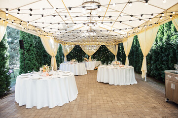 Evening decoration of a wedding party. Tables for guests with a garland and lamps