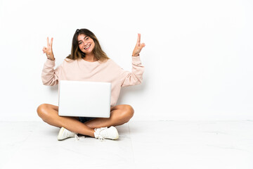 Naklejka premium Young woman with a laptop sitting on the floor isolated on white background showing victory sign with both hands
