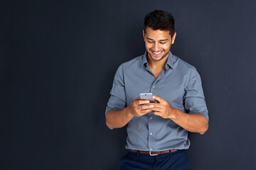Staying informed with all his business connections. Studio shot of a young businessman texting on a cellphone against a dark background.