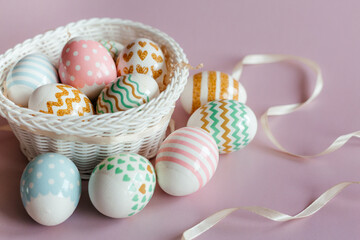 Easter eggs in pastel colors with a pattern in white basket on pink background.