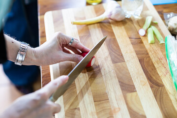 Woman cuts radishes on cutting board on wooden table