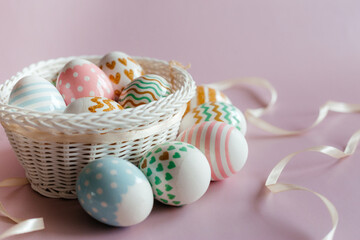 Easter eggs in pastel colors with a pattern in white basket on pink background.