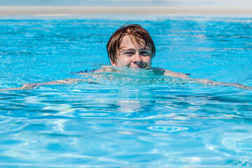 cute handsome teenage boy swims in the pool