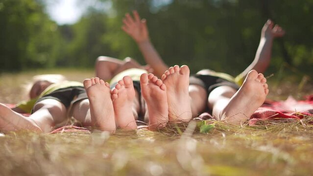 happy family. close-up of a kids leg feet lie on the grass in the summer park. children feet close-up team together happy childrens friendship sun. children lie in the park on the grass family